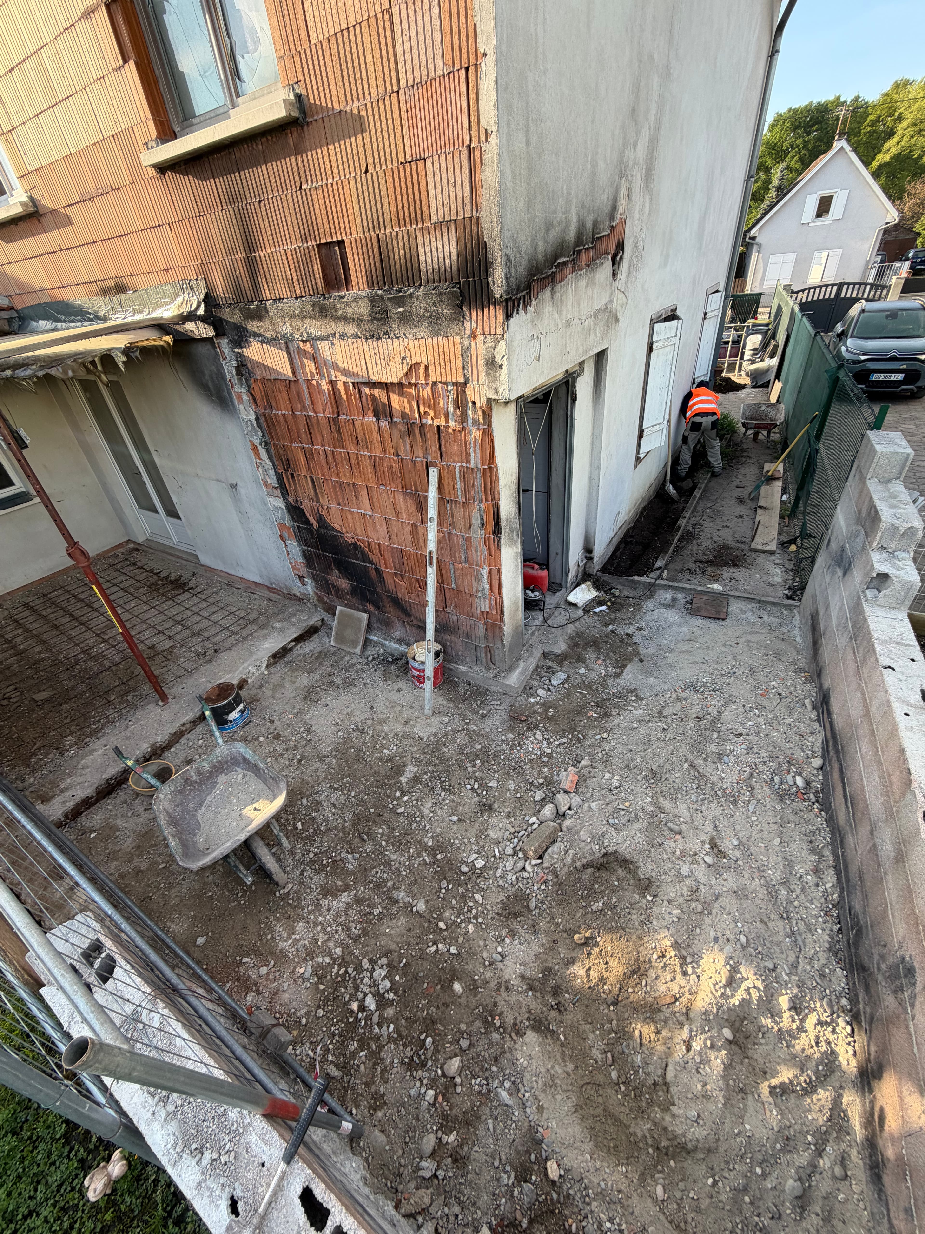 Mur de façade piqué après incendie, briques mises à nu, cour en cours de terrassement.